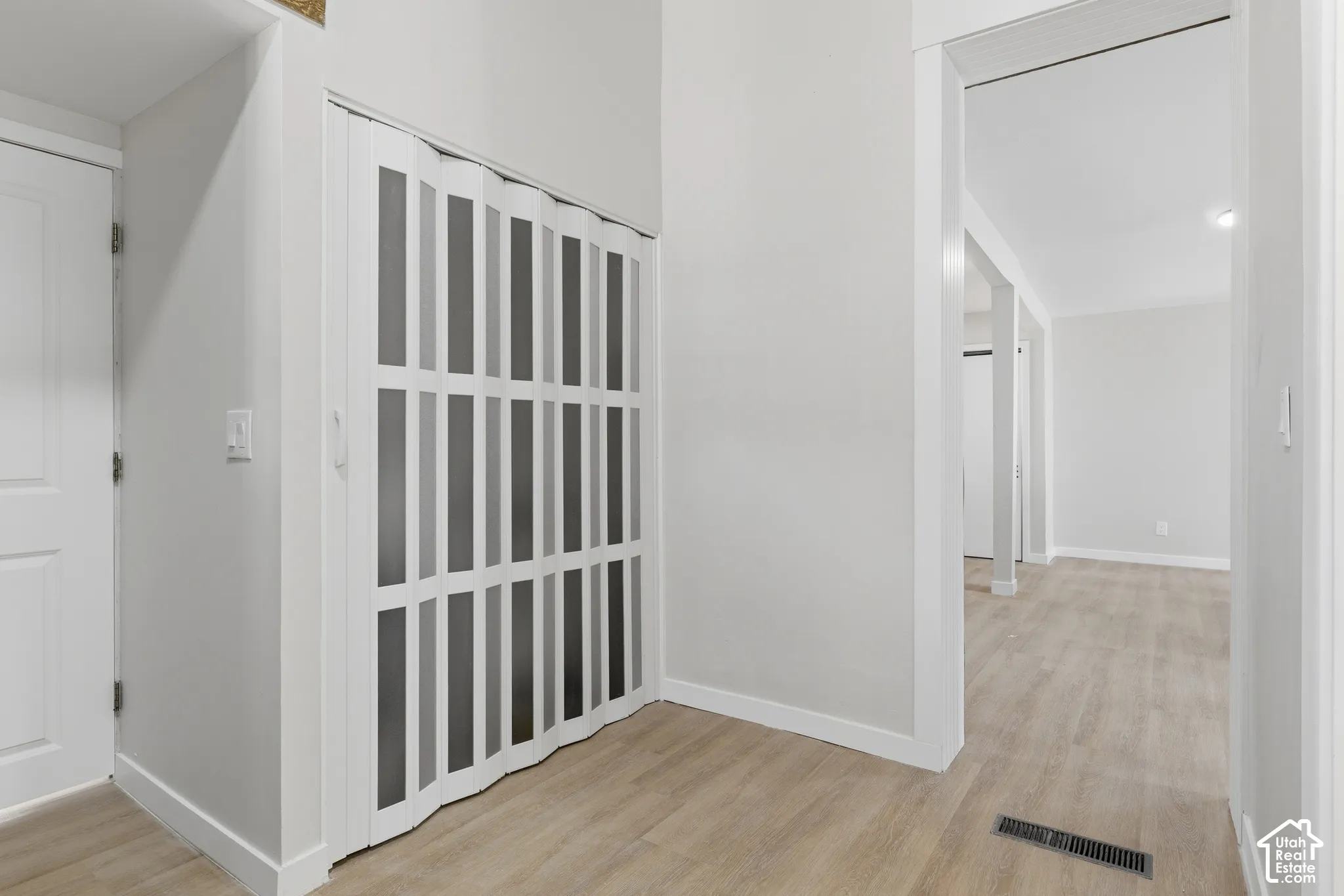 Interior hallway featuring wood-finish flooring, white baseboards, and a white accordion door with frosted panels