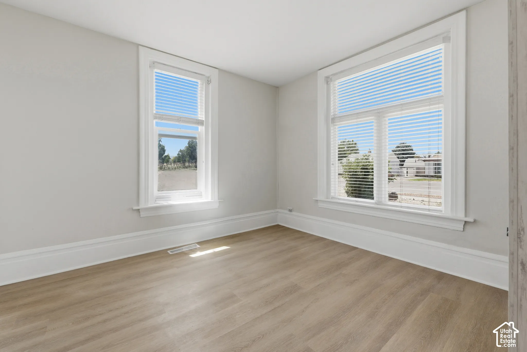 Bright room featuring two windows with white blinds, wood-finish flooring, white baseboards, and light gray walls