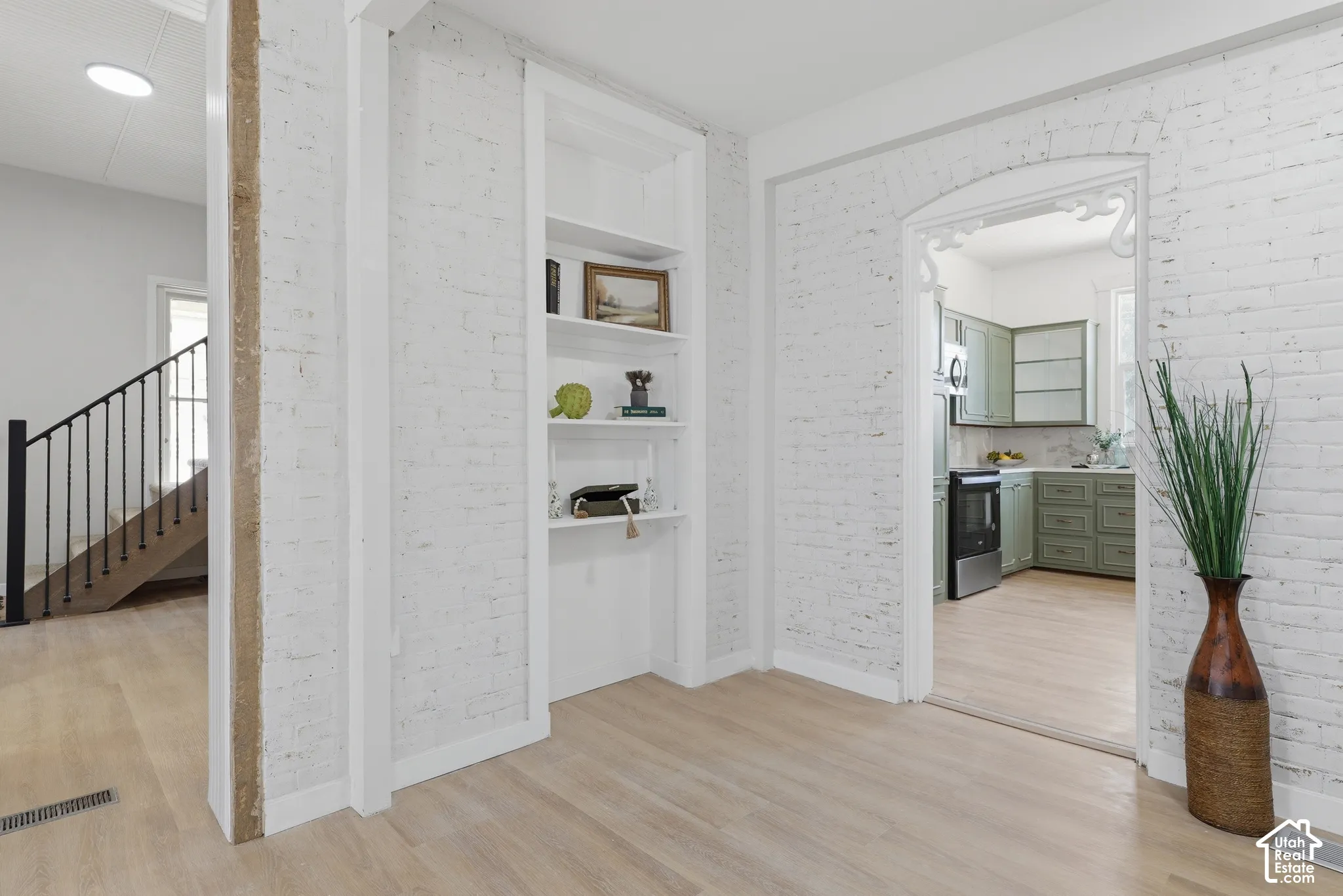 Interior space featuring white-painted brick walls, light wood-finish flooring, and a built-in shelving unit