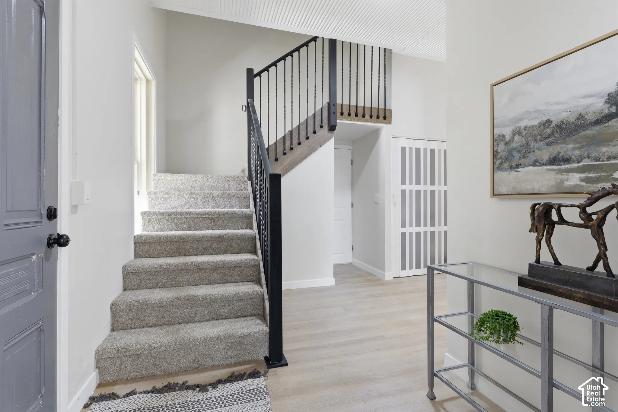 Entryway featuring a carpeted staircase with a wrought iron railing, light wood-finish flooring, and white paneled walls