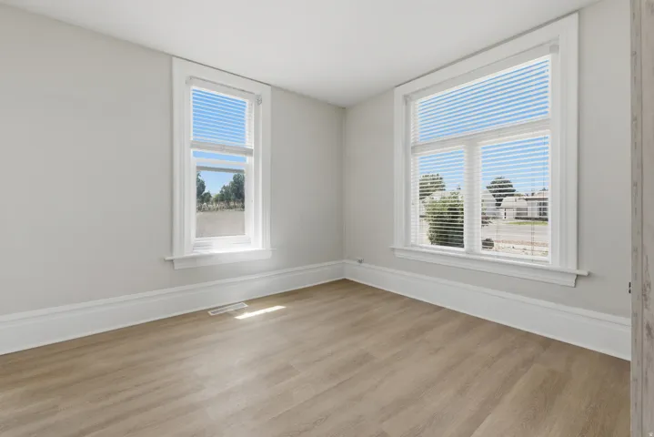 Bright room featuring two windows with white blinds, wood-finish flooring, white baseboards, and light gray walls