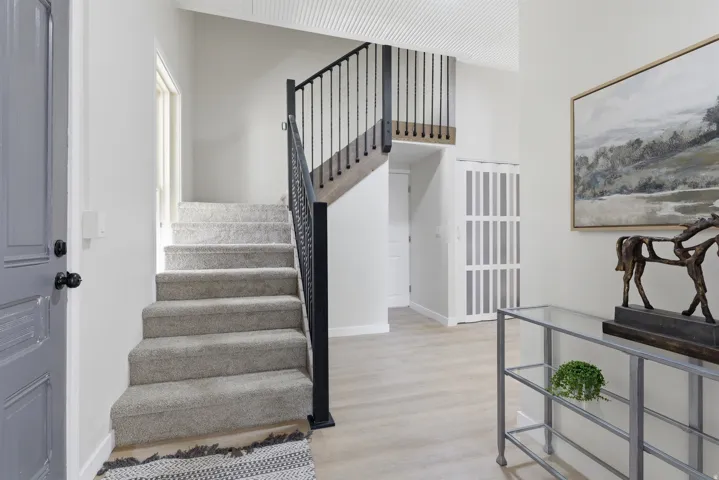 Entryway featuring a carpeted staircase with a wrought iron railing, light wood-finish flooring, and white paneled walls