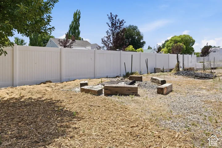 Outdoor space featuring a fire pit area with timber seating, a white privacy fence, and a gravel ground cover