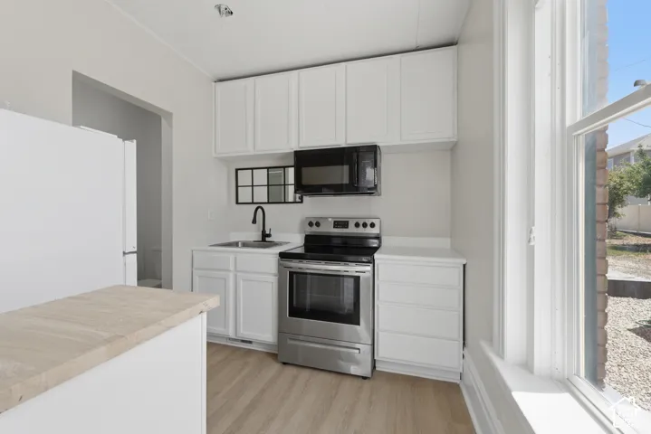 Kitchen featuring white cabinetry, stainless steel range and microwave, light wood-finish flooring, and a white countertop with an undermount sink and matte black faucet