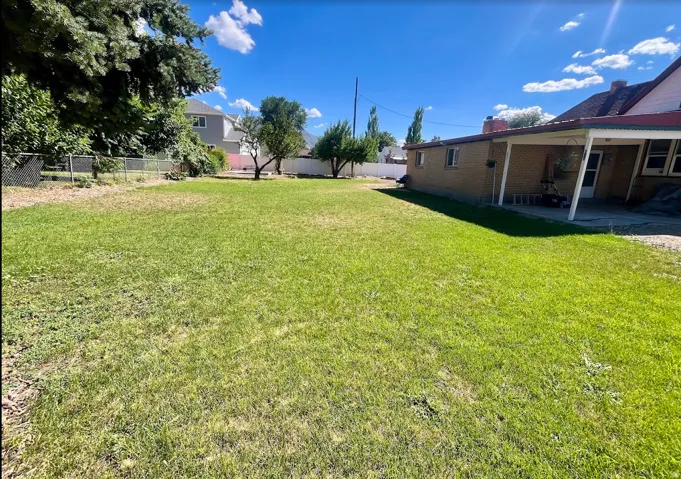 Expansive rear yard featuring a large grass lawn, mature trees, and a covered patio area