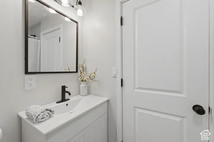 White vanity with an integrated sink and matte black faucet, complemented by a rectangular framed mirror and three-light vanity fixture