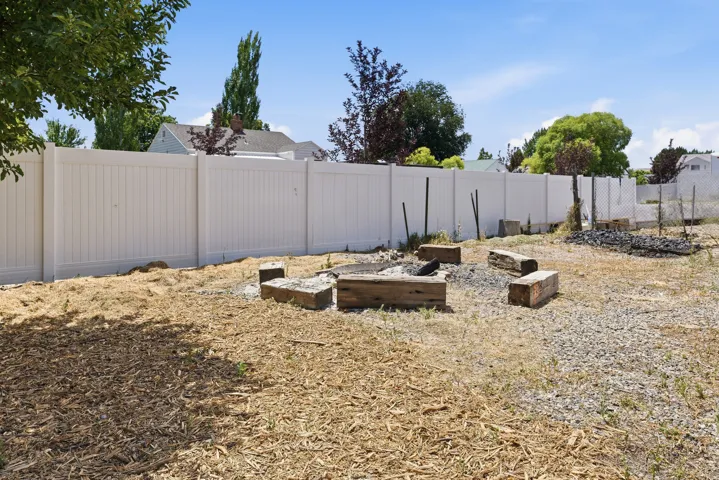 Outdoor space featuring a fire pit area with timber seating, a white privacy fence, and a gravel ground cover