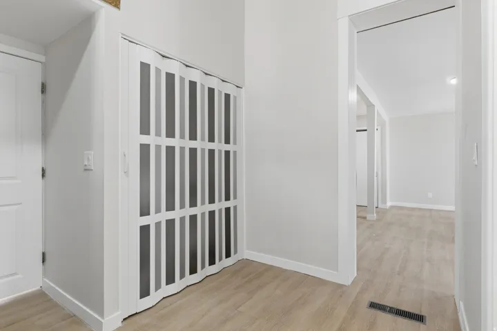 Interior hallway featuring wood-finish flooring, white baseboards, and a white accordion door with frosted panels