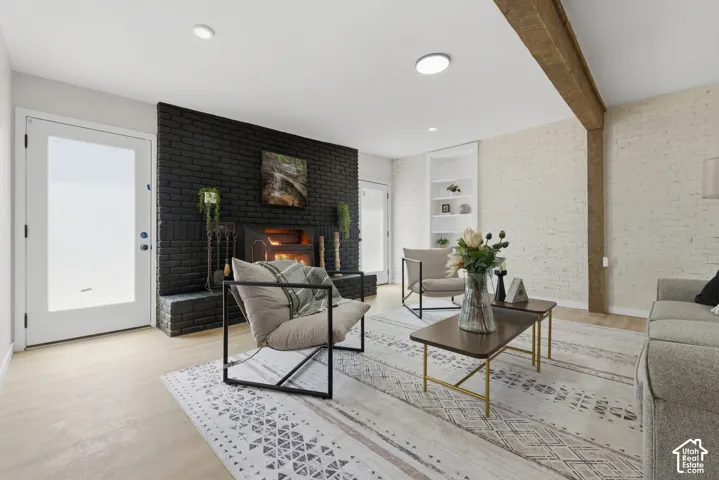 Spacious living area featuring a black brick fireplace, recessed lighting, wood-finish flooring, a white brick accent wall, and built-in shelving