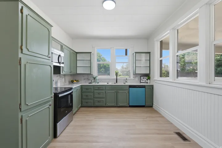 Kitchen featuring sage green cabinetry, stainless steel oven and microwave, light wood-finish flooring, white beadboard wall paneling, and multiple windows