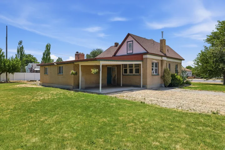 Brick exterior with a covered patio, a gravel driveway, and a spacious lawn