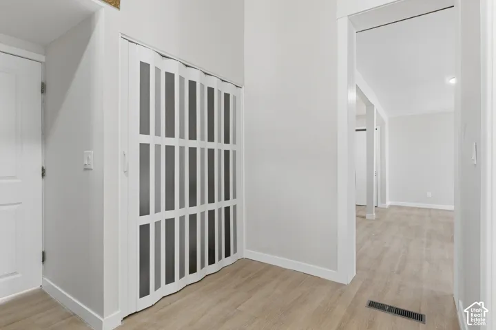 Interior hallway featuring wood-finish flooring, white baseboards, and a white accordion door with frosted panels