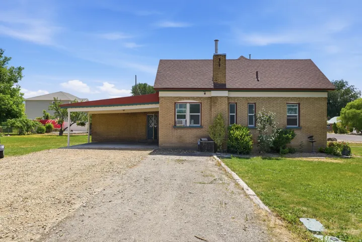 Brick exterior featuring a covered carport, pitched roof, and a gravel driveway
