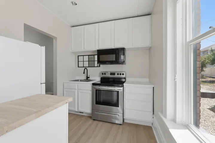 Kitchen featuring white cabinetry, stainless steel range and microwave, light wood-finish flooring, and a white countertop with an undermount sink and matte black faucet
