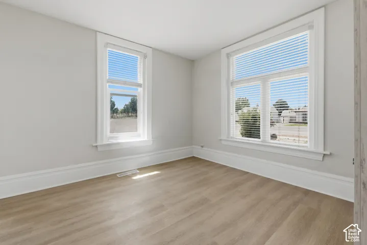 Bright room featuring two windows with white blinds, wood-finish flooring, white baseboards, and light gray walls