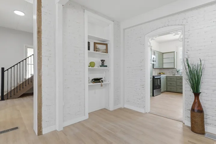 Interior space featuring white-painted brick walls, light wood-finish flooring, and a built-in shelving unit