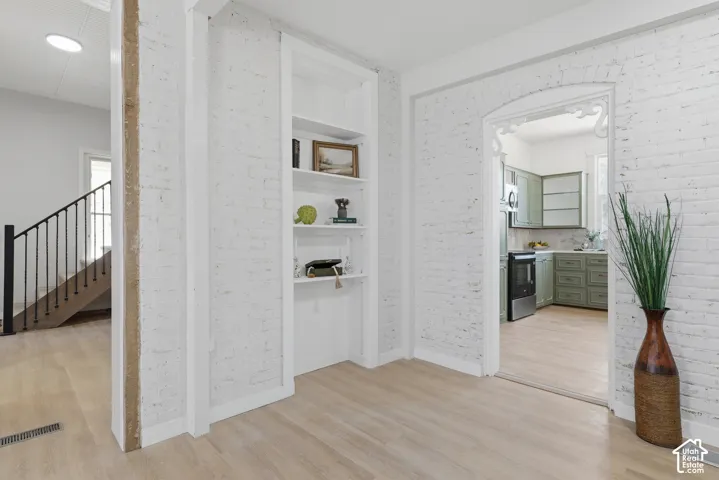 Interior space featuring white-painted brick walls, light wood-finish flooring, and a built-in shelving unit
