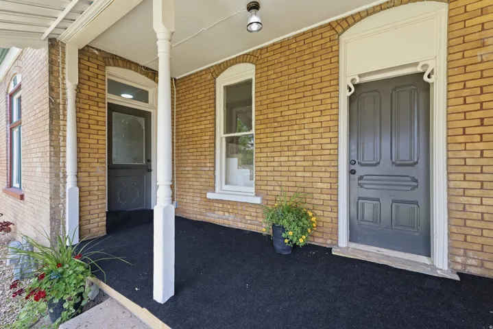 Brick facade featuring an arched entryway with decorative trim, a paneled door, and a covered porch