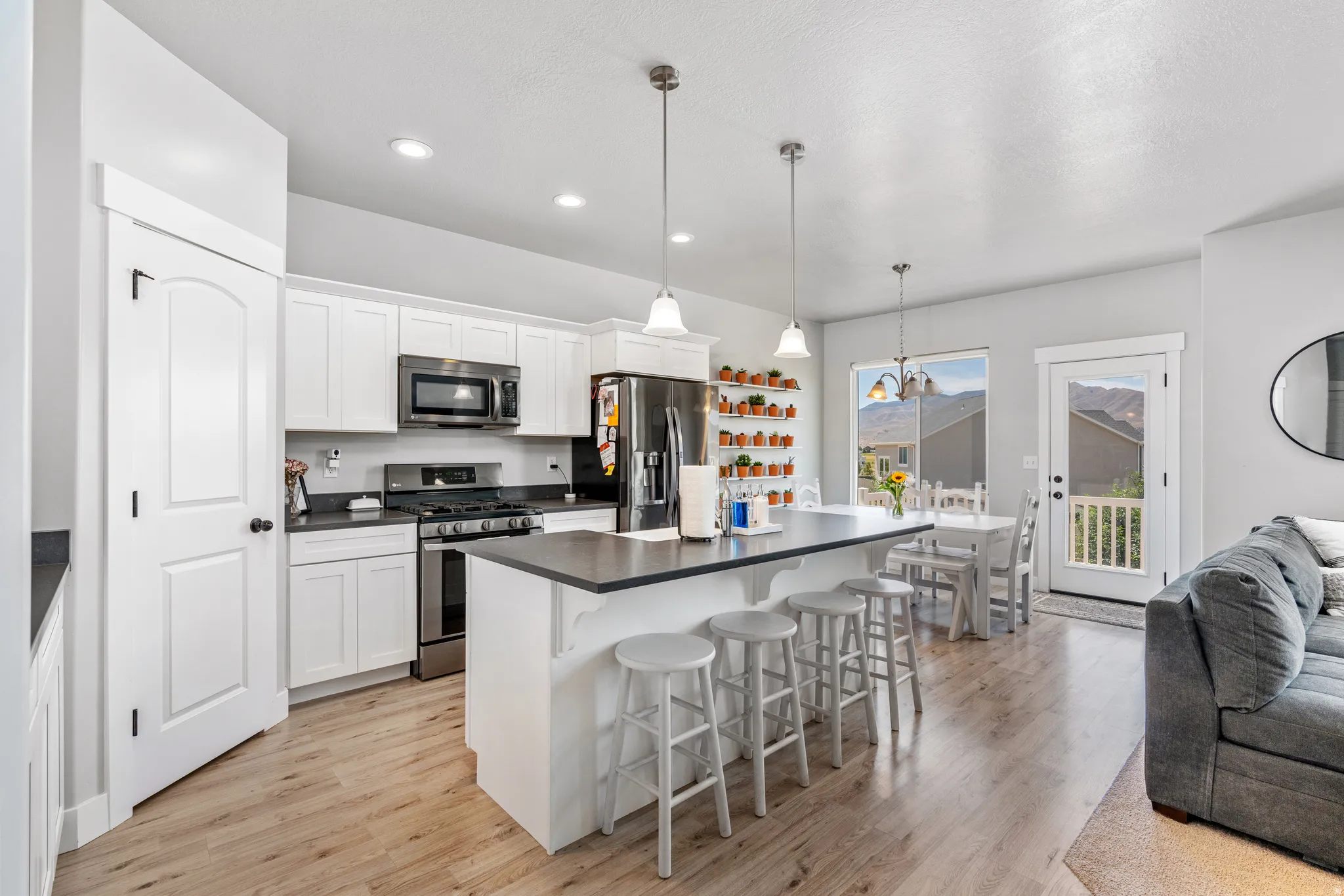 Open-concept kitchen featuring white cabinetry, dark countertops, stainless steel appliances, and wood-finish flooring