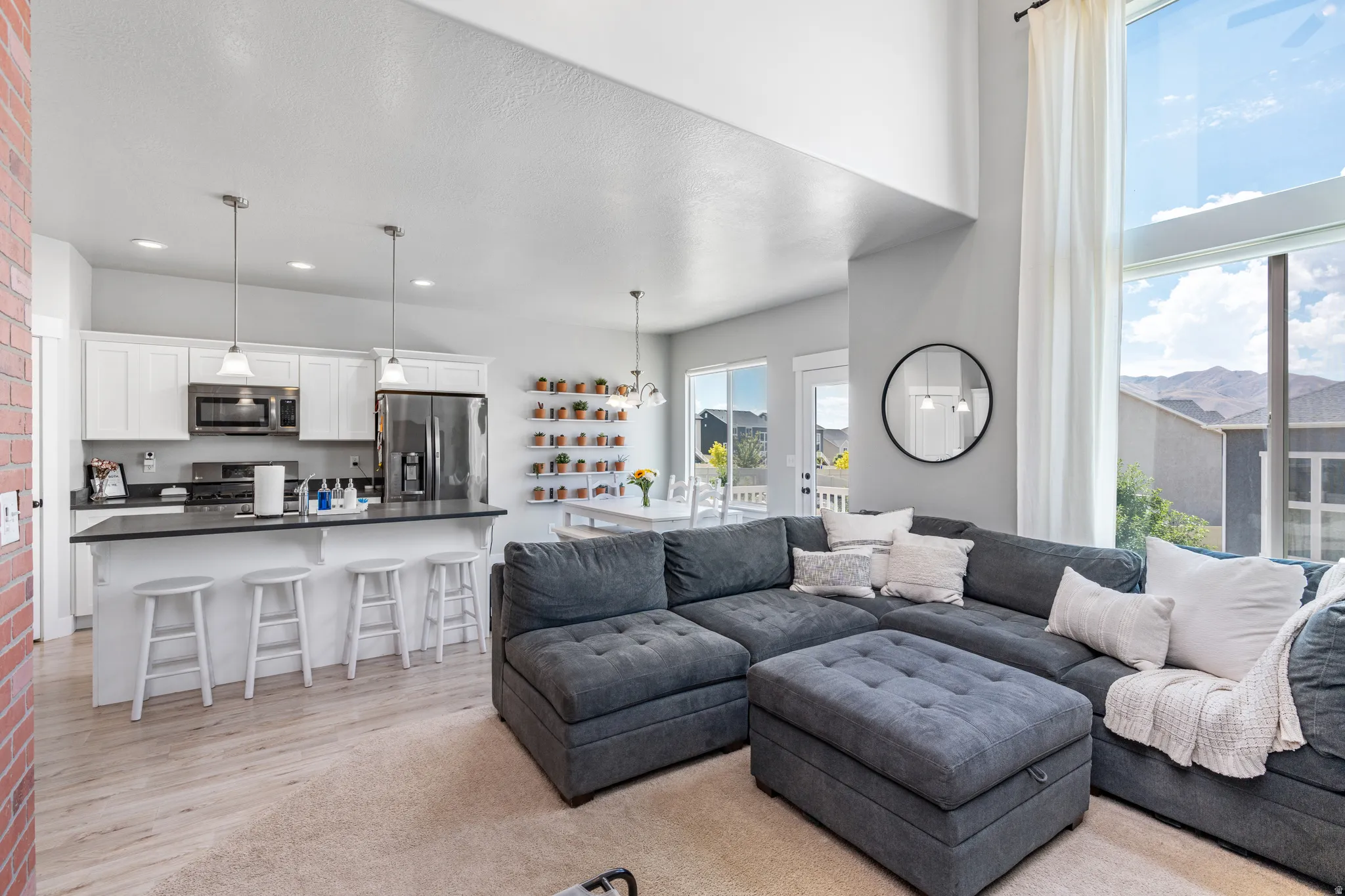 Open-concept living space featuring a two-story window, wood-finish flooring, a kitchen island with pendant lighting, white cabinetry, and stainless steel appliances
