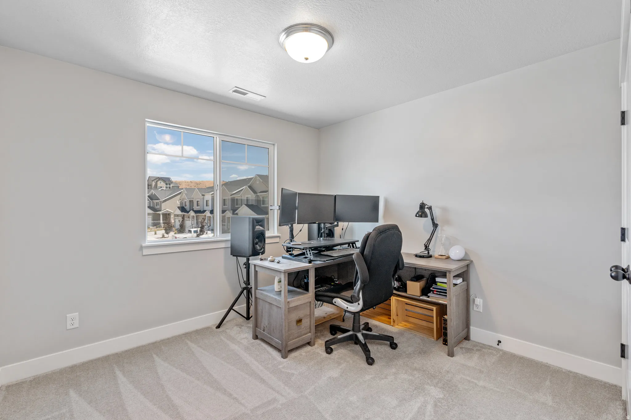 Neutral-toned room featuring a window with white trim, light-colored walls, and textured carpet flooring