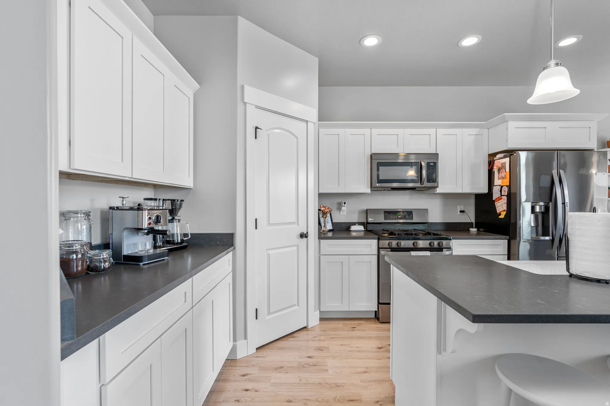 Contemporary kitchen featuring white cabinetry, dark countertops, stainless steel appliances, recessed lighting, and wood-finish flooring