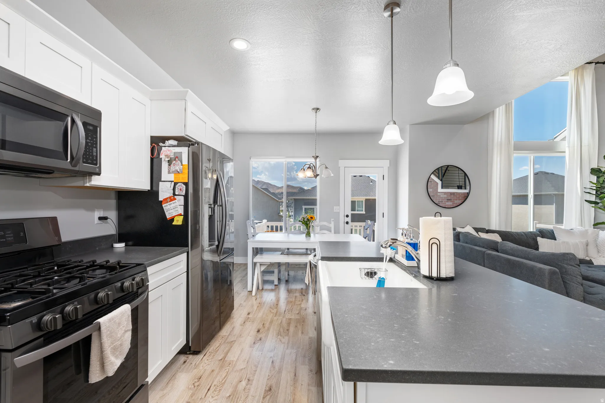 Open-concept kitchen featuring white cabinetry, dark countertops, wood-finish flooring, and stainless steel appliances