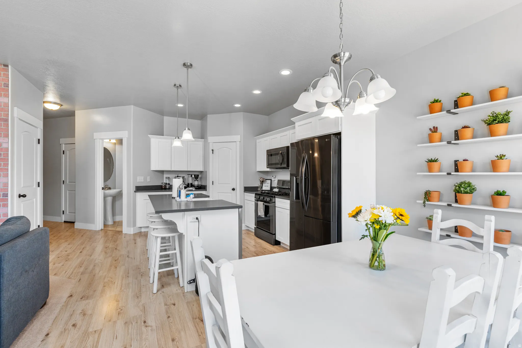 Open-concept living space featuring wood-finish flooring, a kitchen island with seating, white cabinetry, and black appliances