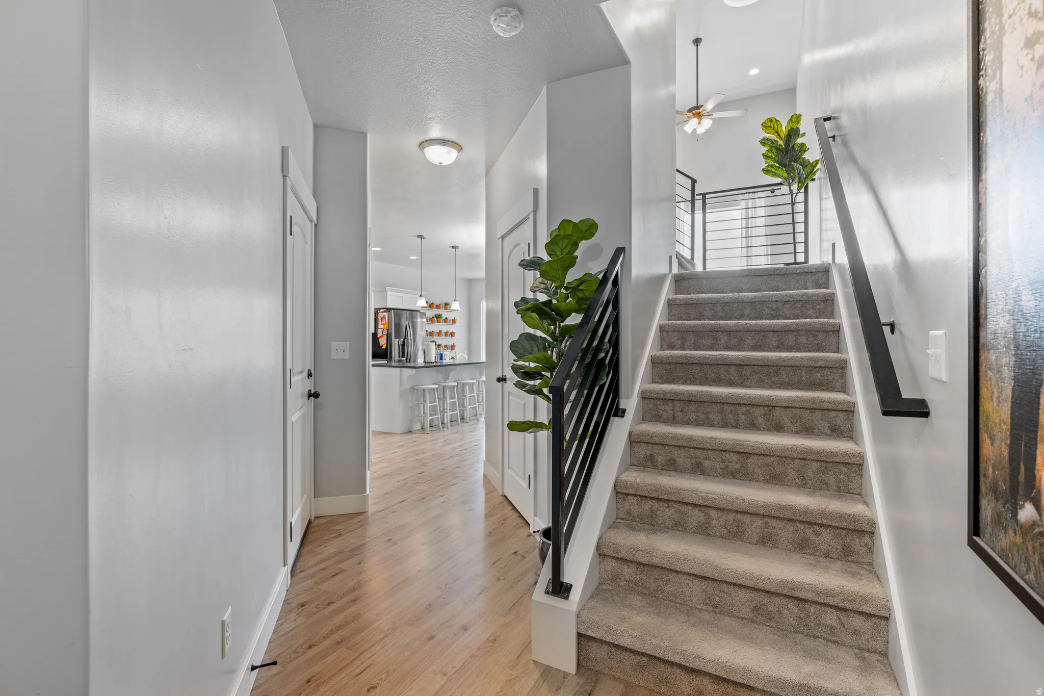 Entryway featuring light wood-finish flooring, a carpeted staircase with modern black railings, white walls, and recessed lighting