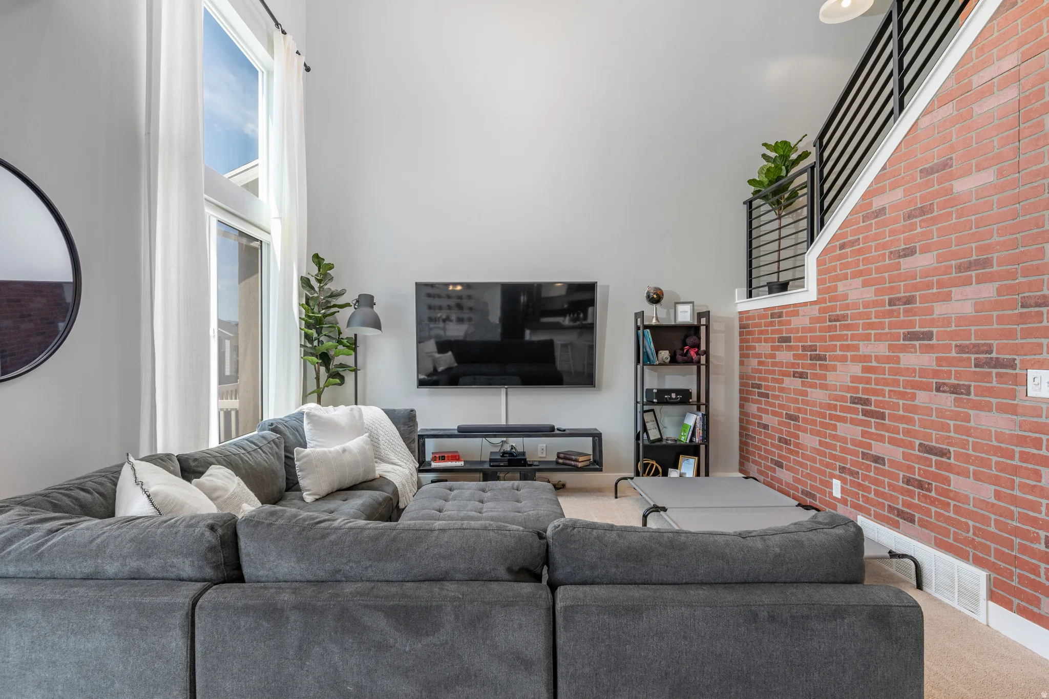 Two-story living area featuring a prominent brick accent wall, high ceilings, and tall vertical windows