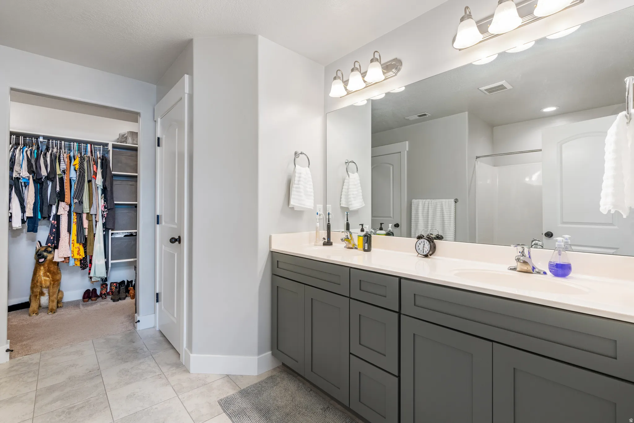 Bathroom featuring a spacious double vanity with gray cabinetry, light-toned countertop, and a large mirror with overhead lighting