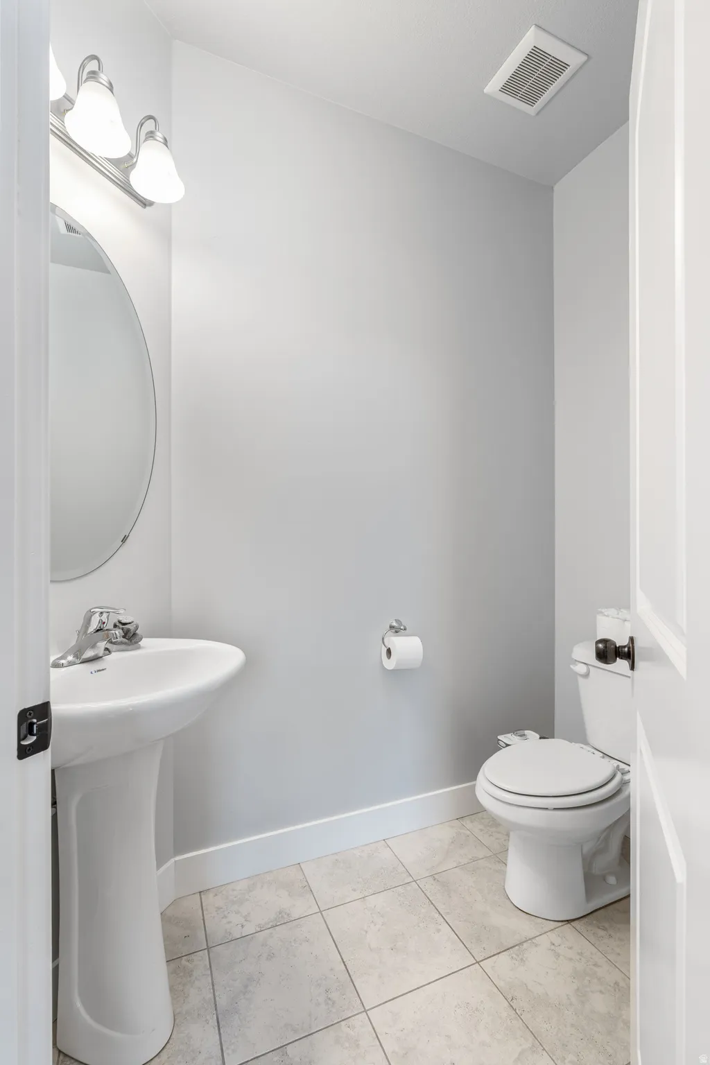 Bathroom featuring a pedestal sink, oval mirror, wall-mounted light fixture, white toilet, and tiled flooring