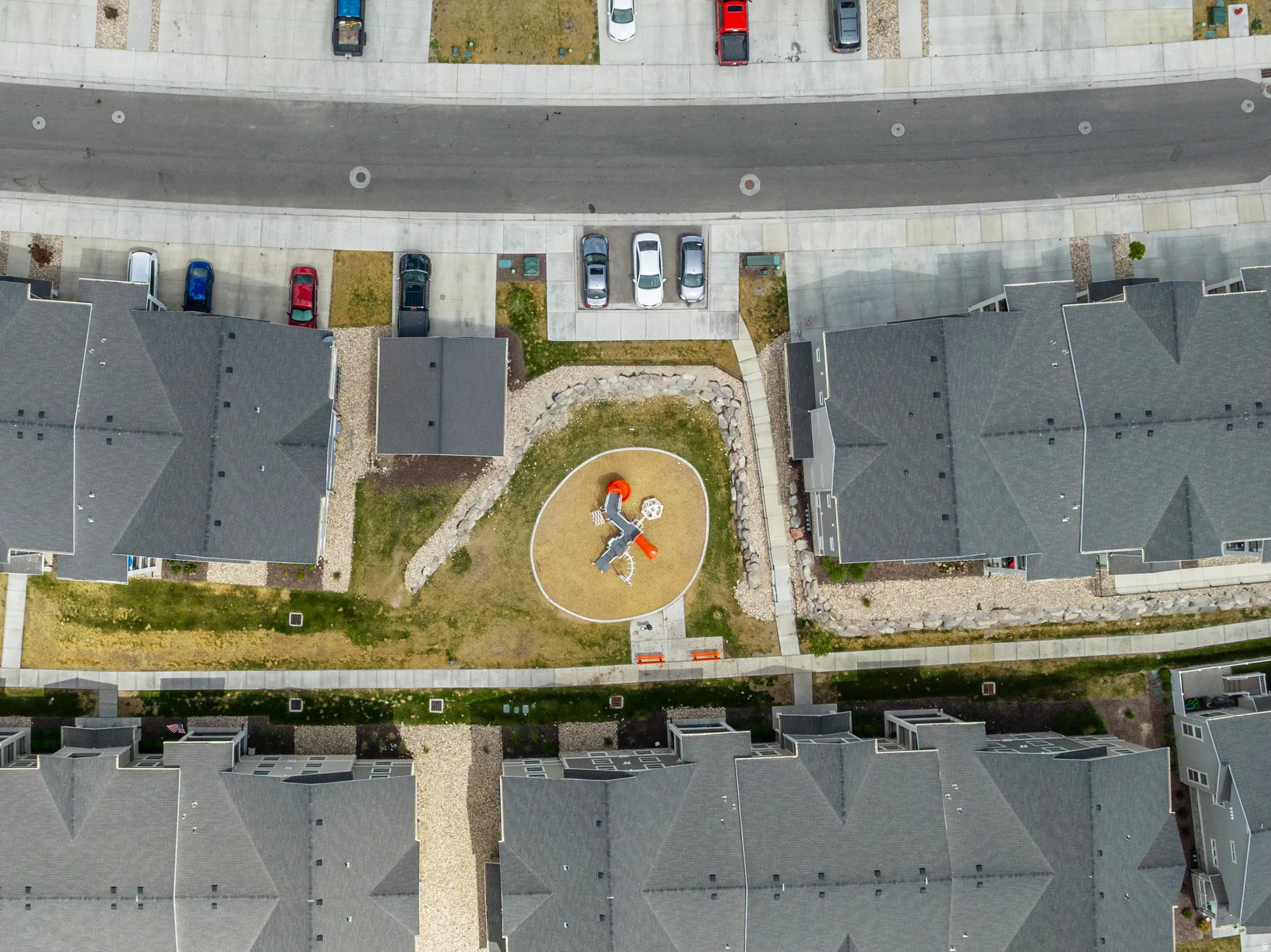 Community green space featuring a playground with a slide, surrounded by a concrete path and landscaped beds