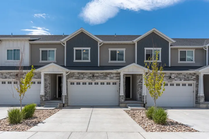 Modern townhome exterior featuring a stone and siding facade, covered entry, attached garage, and concrete driveway