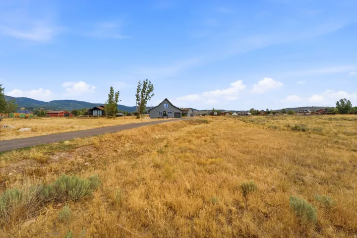 Contemporary gray exterior with a pitched roof, featuring a paved driveway, and surrounded by open, undeveloped land