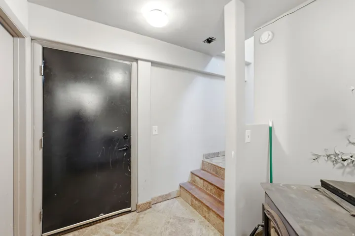 Entry area featuring a dark-paneled door, recessed lighting, and a partial view of interior stairs with stone-finish treads