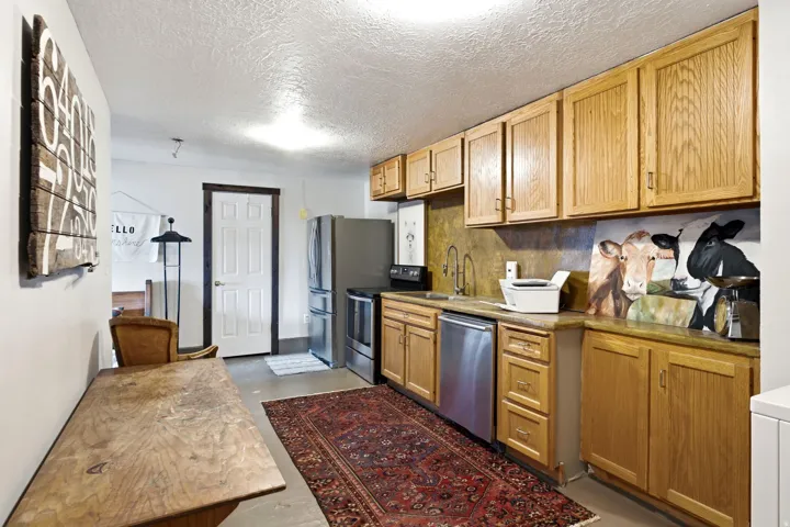 Kitchenette with oak cabinetry, stone-finish countertops, and stainless steel appliances including a refrigerator, range, and dishwasher