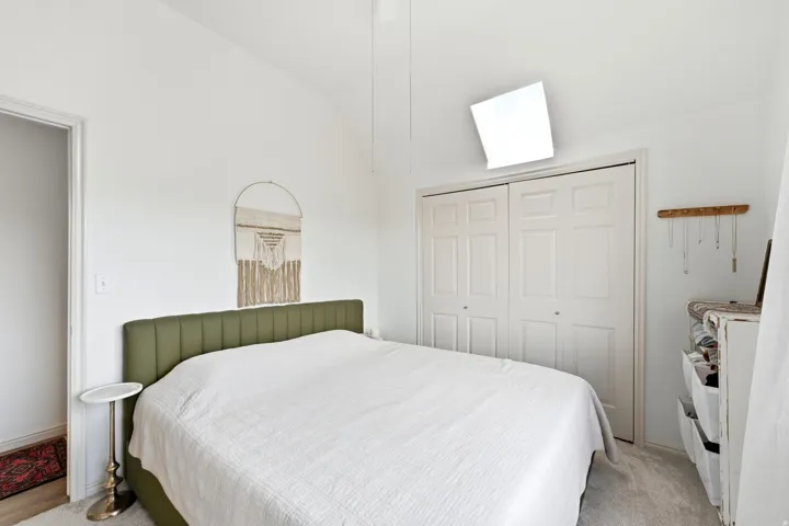 Vaulted ceiling bedroom with light-colored carpeting, white walls, and a bi-fold closet with paneled doors