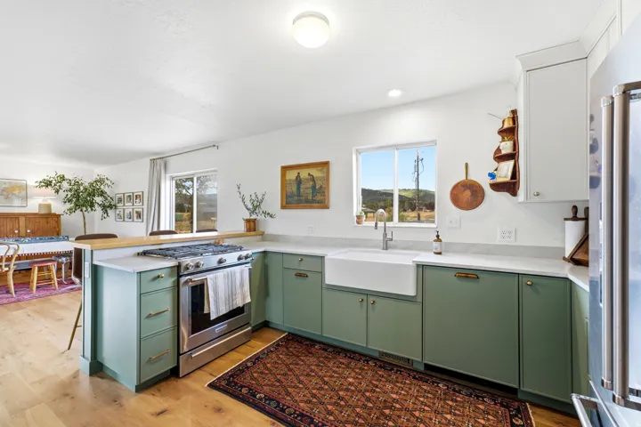 Kitchen featuring sage green lower cabinetry, wood-finish flooring, a farmhouse sink, stainless steel appliances, and light-toned countertops