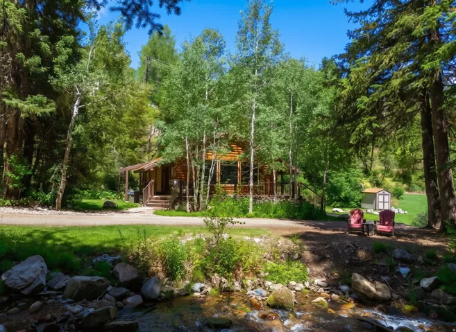 Log cabin exterior featuring a covered porch, wood siding, and mature trees