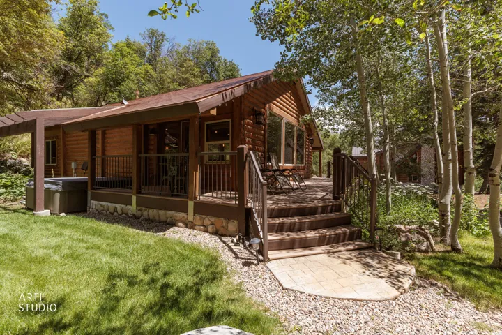 Log-style exterior, wraparound porch, steps down to a concrete patio at the base of the stairs