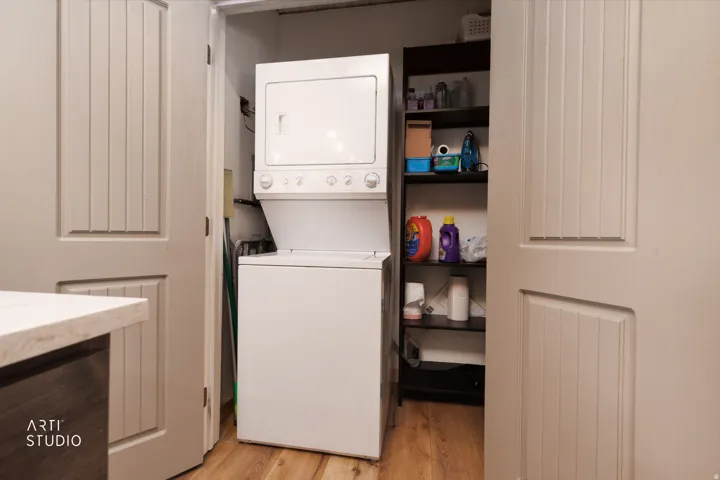 Integrated laundry center with stacked appliances, adjacent built-in shelving.