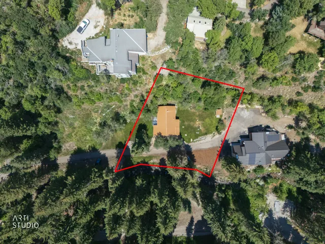 Aerial perspective showcasing a property outlined in red, featuring a single-story residence with a light brown roof, surrounded by mature trees and natural landscaping
