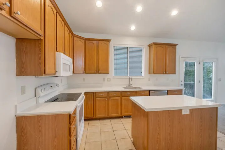 Kitchen featuring light wood cabinetry, white countertops, built-in microwave, white electric range, and a central island