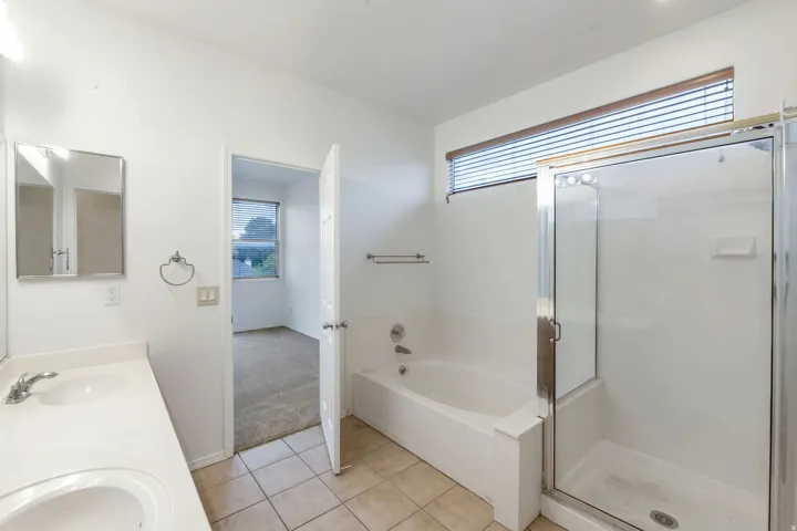 Bathroom featuring a dual vanity with a white countertop, a built-in tub, a separate glass-enclosed shower, and a high horizontal window with blinds