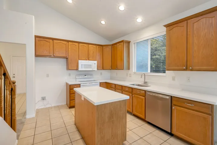 Kitchen featuring a vaulted ceiling with recessed lighting, wood-finish cabinetry, white countertops, stainless steel dishwasher, and a central island