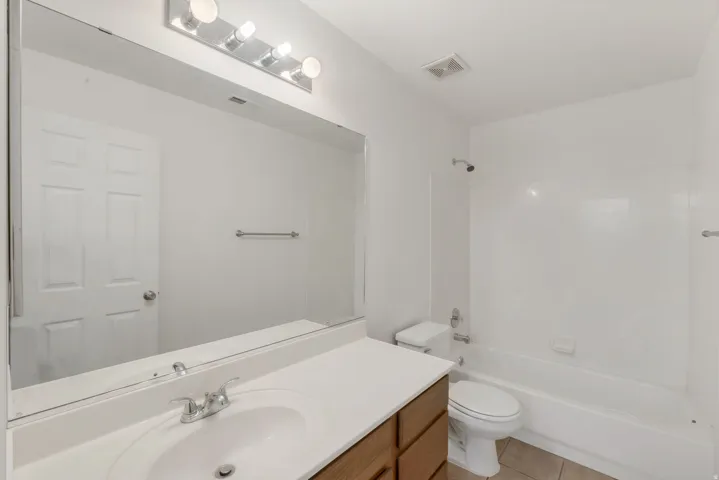 Bathroom featuring a vanity with a white countertop and integrated sink, a large wall-mounted mirror, and a built-in bathtub with shower