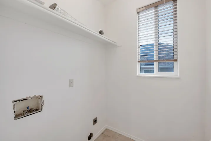 Utility area featuring a single fixed shelf, window with horizontal blinds, and tile flooring