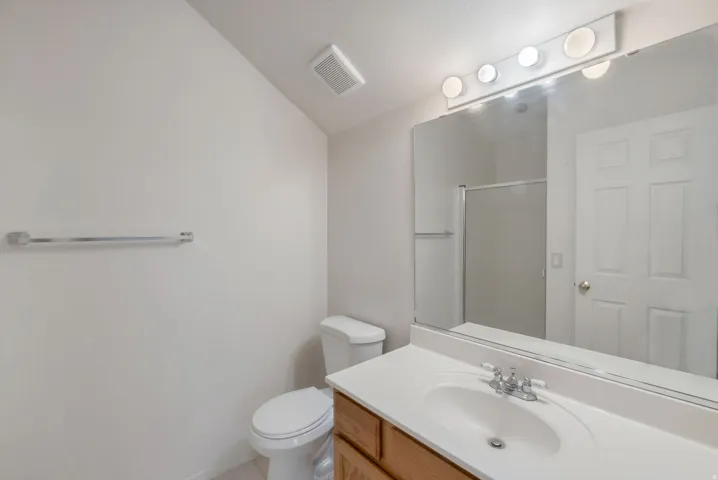 Bathroom featuring a wood-finish vanity with a white countertop, an integrated sink, and a large wall-mounted mirror with overhead lighting