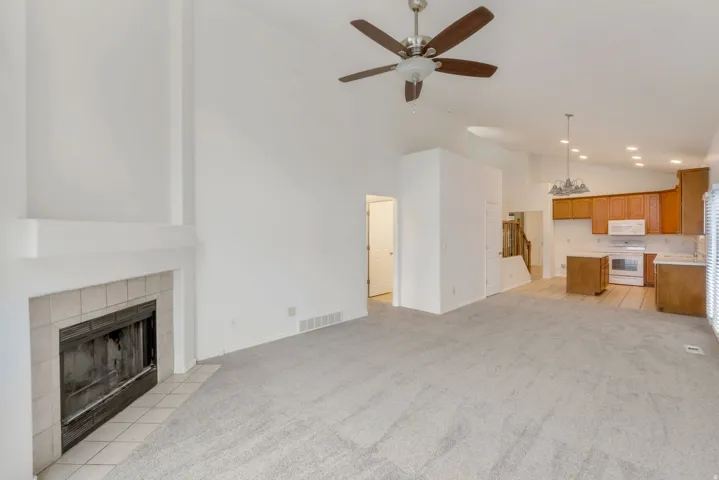 Spacious living area featuring a tiled fireplace with white mantle, vaulted ceilings, and light-toned carpet flooring